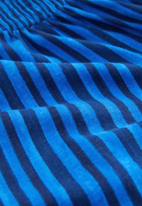 Modrá látka s rovnomerne rozmiestnenými tmavomodrými vertikálnymi pruhmi, ktorá vykazuje záhyby a nariasenú gumu na hornej hrane.