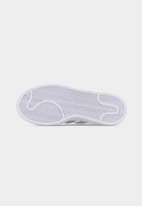Semelle blanche en caoutchouc d'une basket avec des motifs de bande de roulement en zigzag profond et courbes, vue par le dessous sur un fond uni.