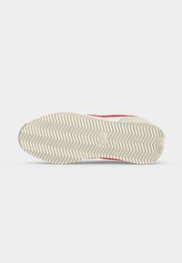 Σόλα από μπεζ και κόκκινο παπούτσι Nike με ζιγκ-ζαγκ σχέδιο πέλματος και μικρό λογότυπο Nike στο κέντρο.