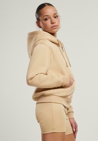 Felpa beige con tasca a marsupio, cappuccio con cordino e polsini a coste. Abbinata a pantaloni corti beige coordinati. Tessuto dal tocco morbido.