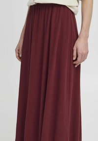 Fustă maxi bordeaux, confecționată dintr-un material moale, cu un talie elastică adunată și o siluetă fluidă, având o textură subtilă.