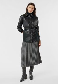 Czarna skórzana koszula z kołnierzykiem, paskiem w talii i zapięciem na guziki. Szara plisowana spódnica midi oraz czarne botki na obcasie. Gładka faktura całości.