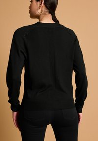 Pulover negru din tricot, cu mâneci lungi, decolteu rotund și tiv cu nervuri. Prezintă detalii texturate de-a lungul cusăturilor umerilor și în mijlocul spatelui.