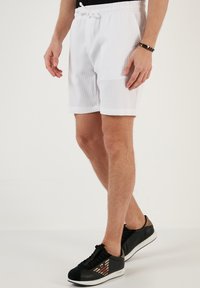 Witte geribde shorts met een elastische tailleband en koord. Gemaakt met zwarte sneakers met accentstrepen en een gestructureerd oppervlak.