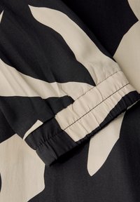 Schwarz-beige gemusterter Stoff mit glatter Textur. Verfügt über einen gerafften Bund mit elastischen Details und kräftigen abstrakten Formen.