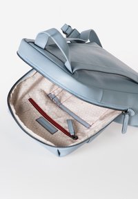 Lichtblauwe leren rugzak met een ritssluiting, die een gestructureerd beige interieur onthult, met rode accenten en georganiseerde compartimenten.