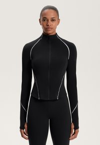 Fekete sportos dzseki, amely testhez álló fazonnal rendelkezik, magas gallérral, teljes hosszúságú cipzárral és szürke fényvisszaverő részletekkel a varrás mentén.