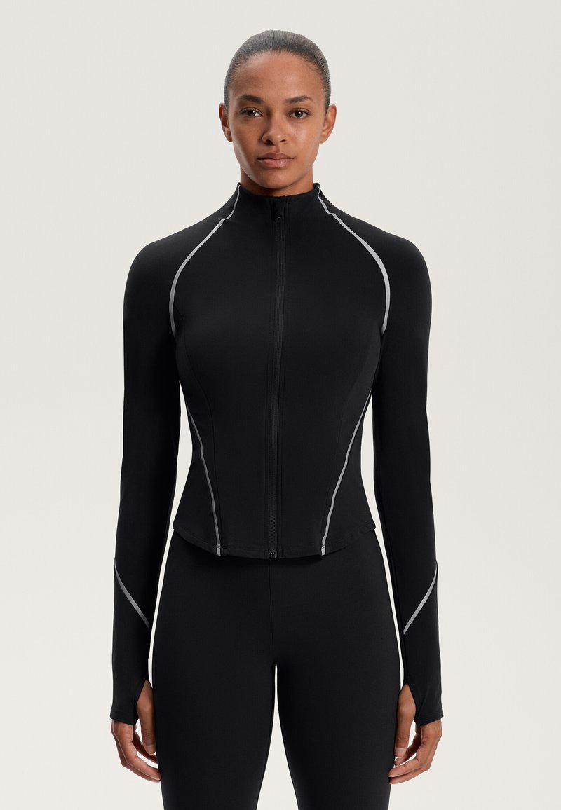 Fekete sportos dzseki, amely testhez álló fazonnal rendelkezik, magas gallérral, teljes hosszúságú cipzárral és szürke fényvisszaverő részletekkel a varrás mentén.