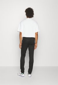 Chemise blanche à manches courtes, pantalon noir slim-fit et baskets de sport blanches avec des accents colorés. Design simple, texture lisse et lignes épurées.