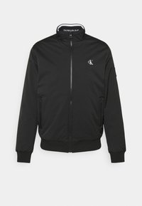 Veste bomber noire en polyester lisse, dotée d'une fermeture éclair, de deux poches latérales, de poignets côtelés et d'un petit logo blanc sur la poitrine.