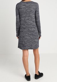 Robe à manches longues bleu marine avec un motif texturé et chiné, coupée droite, assortie à des baskets noires.