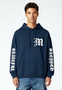 Marineblauwe hoodie met witte grafische tekst "M" op de borst en "GRATEFUL" en "BLESSED" langs de mouwen; bevat een voorzak en een verstelbare capuchon.