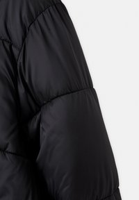 Manche de doudoune noire avec sections horizontales cousues montrant une isolation rembourrée et une texture de tissu lisse.