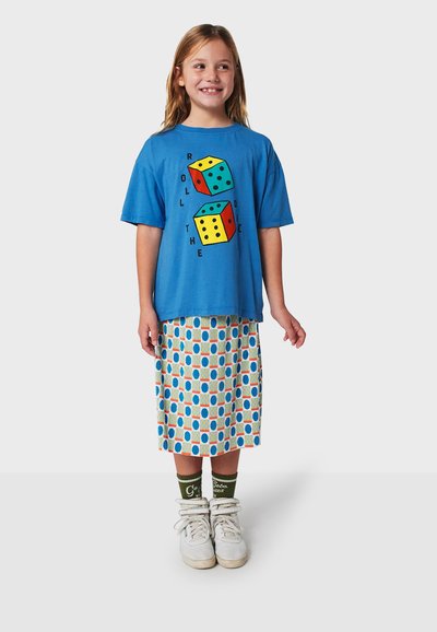 Blue short-sleeve t-shirt with dice graphic and text "ROLL THE DICE"; patterned skirt with circles; white sneakers and green socks.