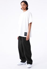 Vit oversized t-shirt med sänkta axlar, med en svart etikett på vänster sida. Matchad med vida svarta byxor och vita sneakers.