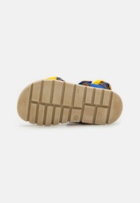 Sandal såle med stripete tekstur, i en lys brun farge, laget av holdbart gummimateriale, med gule, blå og brune aksenter på stroppene.