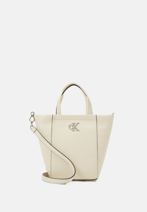 Beżowa torebka Calvin Klein z krótkimi uchwytami, srebrnym logo CK i odpinanym paskiem na ramię, na prostym białym tle.