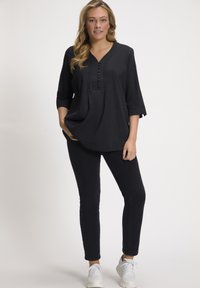 Zwarte button-up tuniek met driekwartmouwen, textuurstof, gecombineerd met slim fit zwarte broek en witte sneakers, die een relaxte pasvorm laat zien.