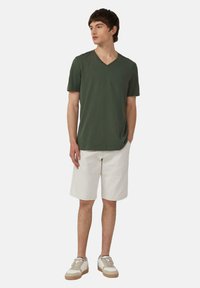 Groene V-hals t-shirt van zacht materiaal, gecombineerd met witte knielange shorts. Model draagt witte en beige sneakers. Eenvoudige, casual stijl.