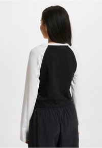 Black and white long-sleeve top with raglan sleeves. Soft fabric with a round neckline and a relaxed fit. Back view shows solid black design.