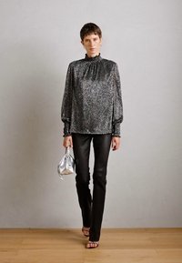 Blusa nera scintillante con maniche a sbuffo e scollatura arricciata, abbinata a pantaloni neri aderenti e una piccola borsa d'argento.