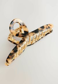 Szpilka do włosów w kolorze tortoise shell z złotymi akcentami, o zakrzywionym kształcie i ozdobnych wycięciach dla dekoracyjnego wyglądu. Lśniące wykończenie i mocny zamek.