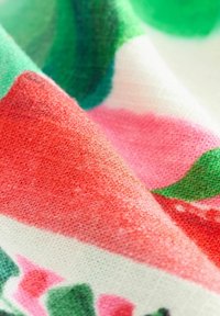 Katoenen stof met abstracte patronen in tinten van rood, roze, groen en wit, met een gladde, gestructureerde oppervlakte.