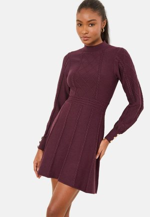 Lila Strickkleid mit langen Ärmeln, das strukturierte Rautenmuster, eine taillierte Passform und Knopfdetails an den Ärmeln aufweist.