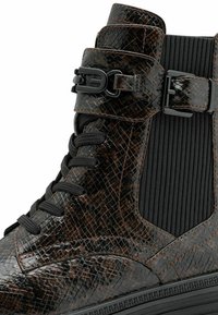 Black and brown patterned ankle boot featuring a glossy reptile-like texture, lace-up design, elastic side panel, and buckle detail.