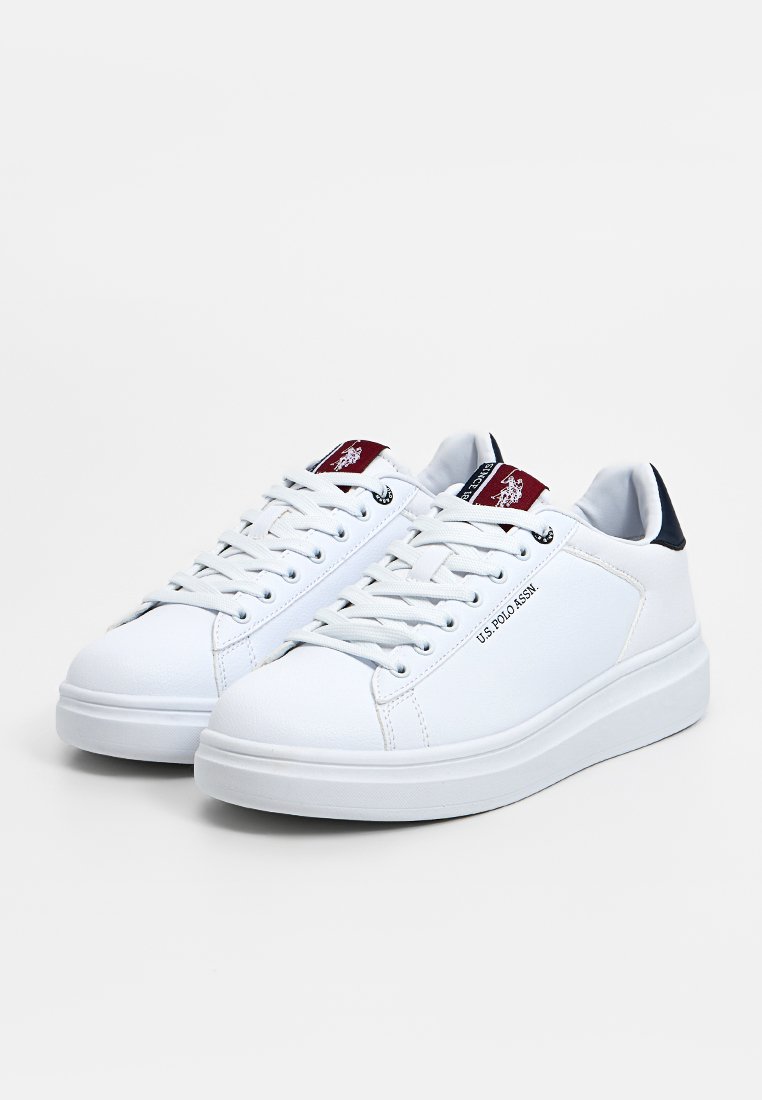 Zapatillas blancas de fibra sintética con cordones y un cuello acolchado, que presentan un acento azul marino en el talón y un parche de logotipo rojo en la lengüeta.