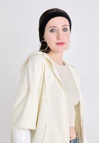 Lys beige zip-up hettegenser med vide ermer, laget av myk stoff, med en frontlomme og snorhette, kombinert med en beige topp.