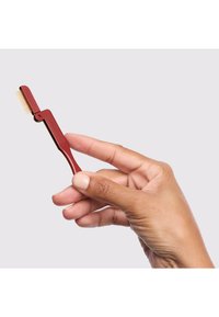 Strumento per la cura dal colore rosso tenuto in mano, con un pettine da un lato e una maniglia curva, progettato per dettagli di precisione o per pettinare capelli.