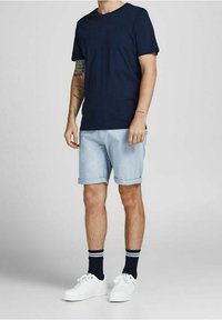 Námorně modré bavlněné tričko, světle modré zrolované šortky, bílé tenisky s černobílými pruhovanými ponožkami a viditelné tetování na ruce.