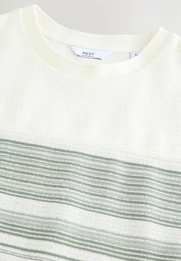 Chandail blanc avec un haut texturé et un panneau rayé horizontal vert. Col côtelé et design à coupe régulière. Étiquette de marque visible.