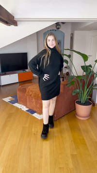 Svart genserkjole med høy hals, ribbet kant og lange ermer. Kombinert med svarte kraftige støvler, stående på tregulv nær en plante.