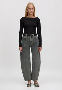 Zwarte top met lange mouwen gecombineerd met hoogpantsgrijze wijde jeans. Model draagt zebra-print schoenen, met een zwarte riem met zilveren hardware.