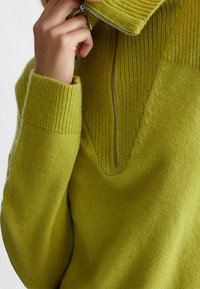 Maglione lavorato a maglia di un vivace verde lime, con colletto alto dotato di zipper, texture a coste sui polsini e colletto, e un design a profonda scollatura a V.