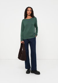 Green long-sleeve sweater with a round neckline, worn with dark blue wide-leg pants and a brown suede shoulder bag. Black platform shoes.