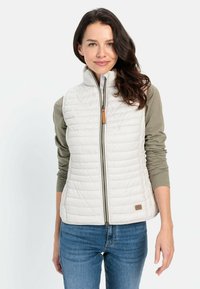 Leichte, cremefarbene, gesteppte Weste mit hohem Kragen, Frontreißverschluss und Lederakzent am Saum. Trägt man über einem grünen Langarmshirt.