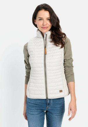 Lichte, crèmewitte gewatteerde vest met een hoge kraag, een ritssluiting aan de voorkant en een leren accent nabij de zoom. Draagt over een groene langemouwen shirt.