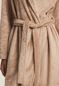 Close-up of a person wearing a soft beige bathrobe tied with a matching fabric belt around the waist.