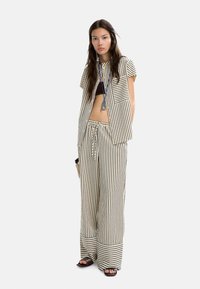 Completo a due pezzi a righe in beige e marrone scuro. Camicia a maniche corte con tasca, pantaloni larghi con vita regolabile e orlo in risalto.
