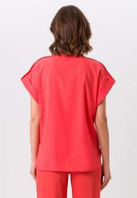 Koraalkleurige blouse met korte mouwen, een relaxte pasvorm, gladde textuur en ronde zoom. Geen zichtbare patronen of accenten.