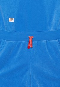Blue fleece tracksuit bottom with a drawstring waist in contrasting red. Features a Nike logo label on the left side. Soft texture, casual design.