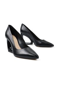 Para czarnych skórzanych szpilek z wydłużonymi noskami i pustymi obcasami na białym tle.