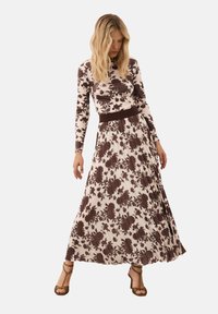 Bruine maxi jurk met bloemenpatroon, een aansluitende bovenkant en lange mouwen, met een geplooide rok en een bruine tailleband.