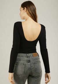 Body noir à manches longues avec un décolleté plongeant dans le dos, associé à un jean en denim gris clair taille haute avec une étiquette marron et deux poches arrière.
