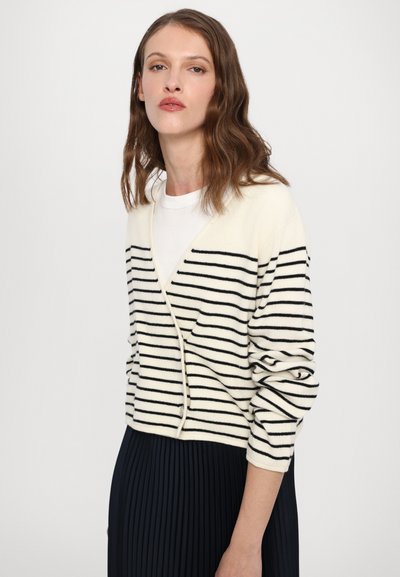Cardigan crema con strisce orizzontali nere, design a V, maniche lunghe e texture morbida. Indossato sopra una camicia bianca e una gonna nera plissettata.