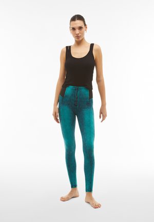 Top in raso nero a costine abbinato a leggings teal a vita alta con una finitura testurizzata e pannelli laterali a contrasto.