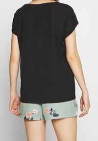 Svart kortärmad topp med lös passform, tillsammans med mintgröna shorts som har blommig broderi i rosa och marinblå färger.